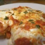 Delicious homemade chicken parmesan with melted cheese and tomato sauce on a white plate.